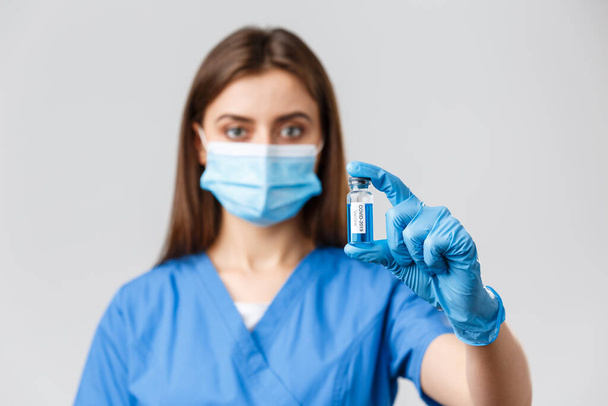 Covid-19, πρόληψη του ιού, της υγείας, των εργαζομένων στον τομέα της υγείας και καραντίνα έννοια. Κοντινό πλάνο ενός σοβαρού νεαρού γιατρού ή νοσοκόμου στην κλινική, που δείχνει το εμβόλιο του κορωναϊού σε φύσιγγα - Φωτογραφία, εικόνα