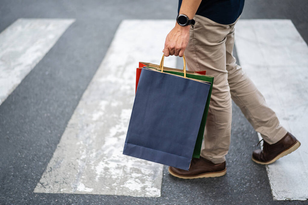 man holding shopping bag walking cross the street in city - 写真・画像