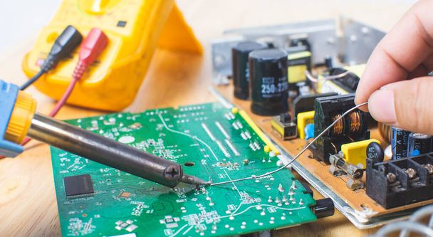 Técnico está utilizando soldador eléctrico y la lata para reparar placa de circuito electrónico
 - Foto, imagen