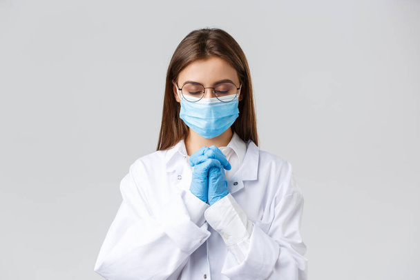Covid-19, preventing virus, health, healthcare workers and quarantine concept. Hopeful doctor in scrubs and medical mask, personal protective equipment, praying with hands clasped together, hope - Fotoğraf, Görsel