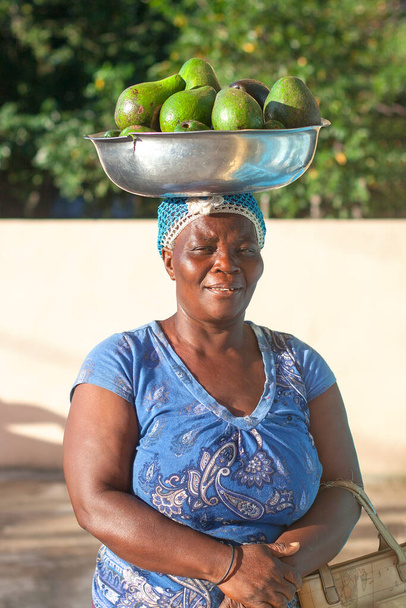 Bayahibe, Dominicaanse Republiek, 31 december 2016, lachende Afrikaanse vrouw met schaal op haar hoofd met rijpe groene avocado 's - Foto, afbeelding