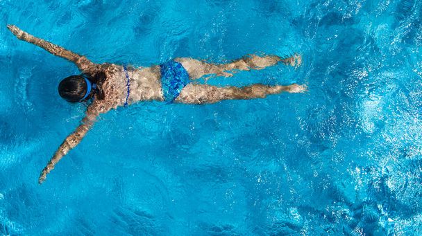 Active girl in swimming pool aerial drone view from above, young woman swims in blue water, tropical vacation, holiday on resort concept - Фото, зображення