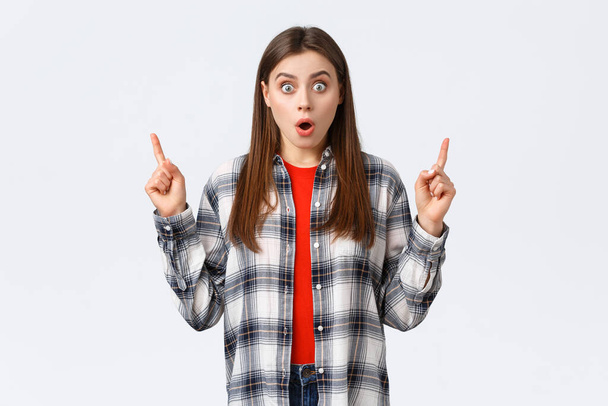 Lifestyle, different emotions, leisure activities concept. Astonished and speechless attractive girl in checked shirt pointing fingers up to tell news, drop jaw staring, make wow expression - Foto, imagen