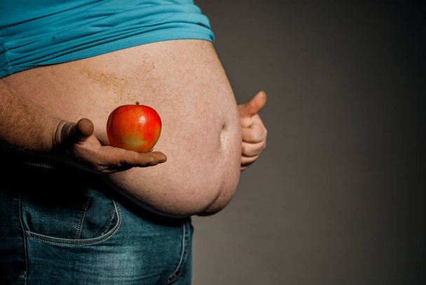 Lihava mies pitelee omenaa paljaan vatsansa edessä. Ruokavalion ja terveellisen ruokavalion käsite. - Valokuva, kuva