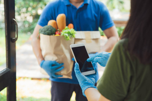Woman appending signature in digital mobile phone after Grocery store delivery man wearing blue shirt delivering food to a woman at home.delivery service during covid19.New normal. - Fotoğraf, Görsel