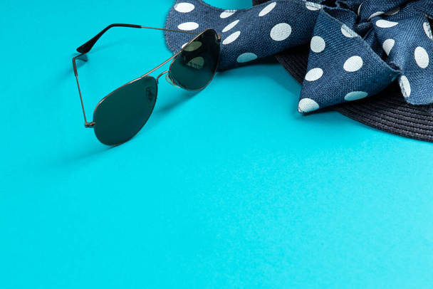 Sombrero azul con cinta y gafas de sol sobre fondo azul. Concepto de verano. Vista superior con espacio de copia
 - Foto, imagen