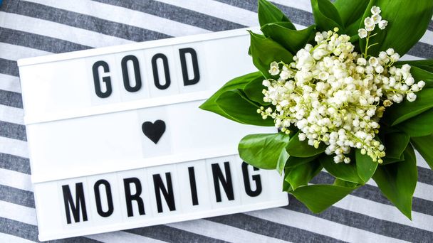 Lightbox with text GOOD MORNING and bouquet lilies of the valley in white bucket, spring time, holiday background - Photo, Image