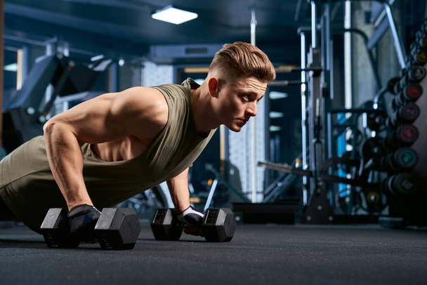 Muscular man doing push ups using dumbbells. - Fotografie, Obrázek
