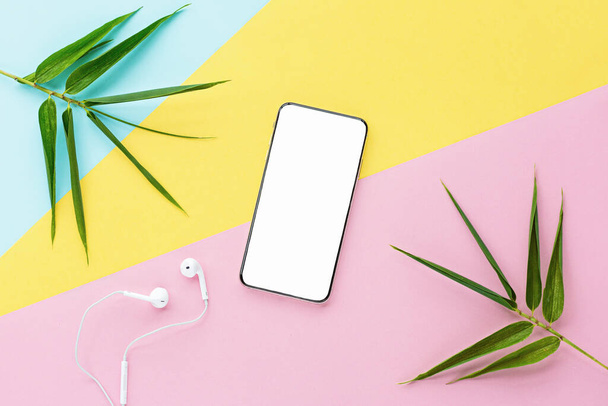 Flat lay top view mockup photo of working space with smartphone, headphones and green leaves on pastel background. Back to school, online education, freelance and home office concept - Φωτογραφία, εικόνα