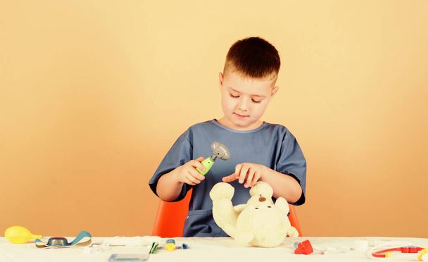 Boy cute child future doctor career. Health care. Kid little doctor busy sit table with medical tools. Medicine concept. Medical procedures for teddy bear. Medical examination. Medical education - Fotó, kép