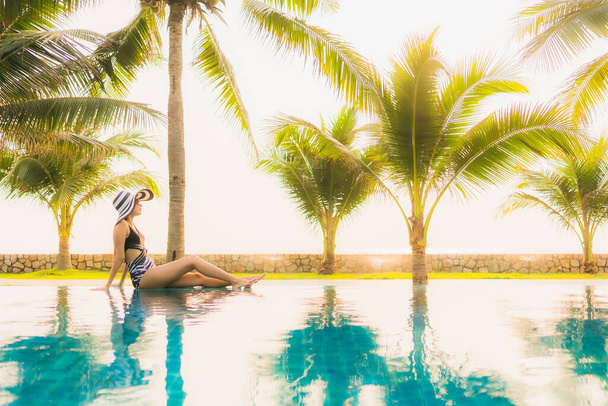 Portret piękna młoda Azjatka relaks wokół odkrytego basenu w ośrodku hotelowym z palmą o zachodzie słońca lub wschodzie słońca na wakacje - Zdjęcie, obraz