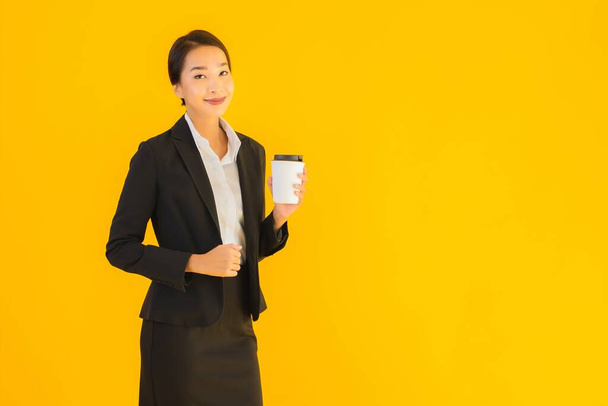 Muotokuva kaunis nuori liike aasialainen nainen älykäs matkapuhelin ja kahvikuppi keltainen eristetty tausta
 - Valokuva, kuva