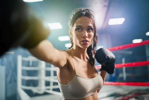 Female boxer showing hit in boxing gloves. - Фото, изображение