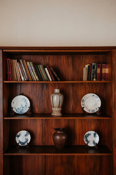 Wooden bookshelf with old books and blue pattern vintage Chinaware plates, Ceramic Vase and copper jar - Foto, Imagen
