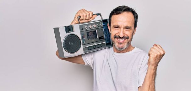 Middle age handsome man listening vintage boombox over isolated white background screaming proud, celebrating victory and success very excited with raised arm - Photo, Image
