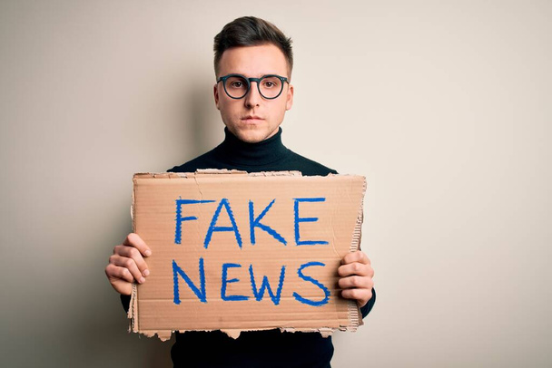 Young handsome caucasian man holding protest carboard for desinformation and fake news with a confident expression on smart face thinking serious - Photo, Image