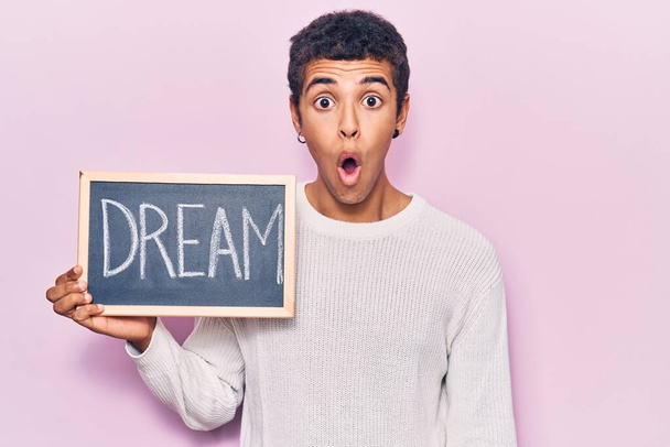 Mladý africký Američan muž drží tabuli se snem slovo vyděšený a ohromený s otevřenými ústy pro překvapení, nevěřící tvář  - Fotografie, Obrázek