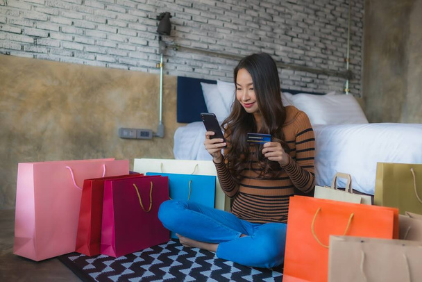 寝室でオンラインショッピングのためのクレジットカードを使用してスマートフォンやノートパソコンのコンピュータを持つ若いアジアの女性 - 写真・画像