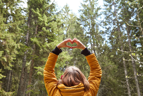 Kalp şeklinde sembolü olan bir kadın doğal ortamda havada duruyor.. - Fotoğraf, Görsel