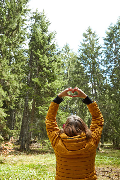 Woman with heart-shape symbol holding up in the air in natural environment. - Photo, Image