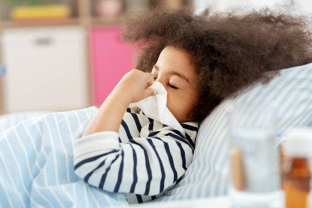 sick girl lying in bed and blowing nose at home - Fotó, kép