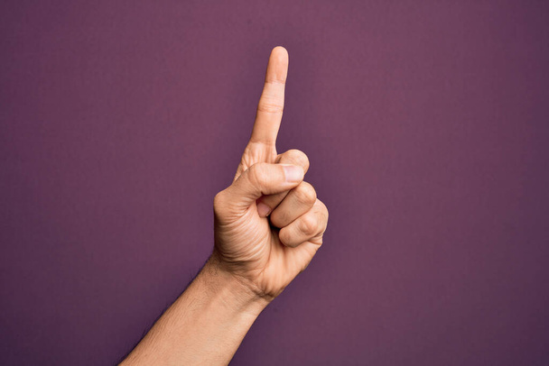 Mano del joven caucásico mostrando los dedos sobre el fondo púrpura aislado contando el número uno usando el dedo índice, mostrando idea y comprensión - Foto, imagen