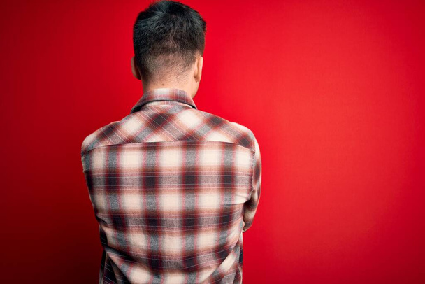 Young handsome caucasian man wearing casual modern shirt over red isolated background standing backwards looking away with crossed arms - Photo, Image