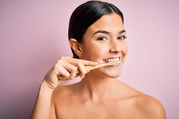 Young beautiful brunette woman brushing her teeth using tooth brush and oral paste, cleaning teeth and tongue as healthy health care morning routine - Fotó, kép