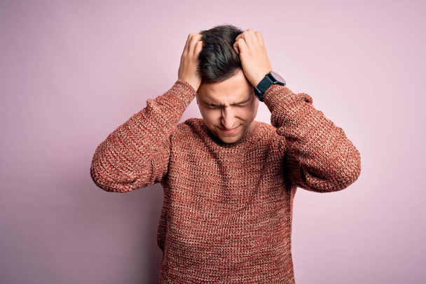 Jeune homme caucasien beau portant un pull d'hiver décontracté sur fond rose isolé souffrant de maux de tête désespérés et stressés parce que la douleur et la migraine. Mains sur la tête. - Photo, image