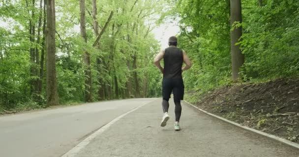 Jonge man met gezichtsmasker in sportkleding op de weg naar Forest. Mannen doen intense run workout - Video