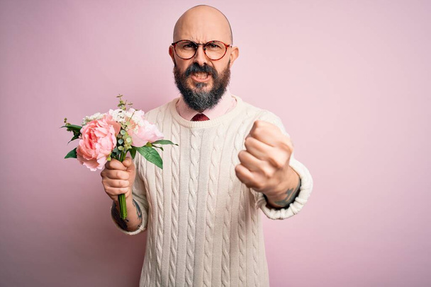 Handsome romantic bald man with beard holding beautiful bouquet over pink background annoyed and frustrated shouting with anger, crazy and yelling with raised hand, anger concept - Photo, Image