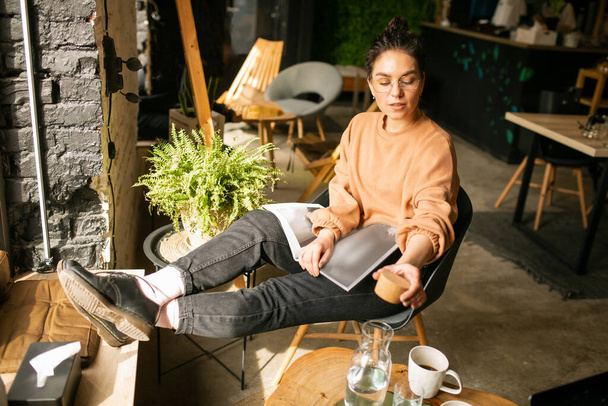  Meisje blogger met een kopje koffie in cafe met tijdschrift - Foto, afbeelding