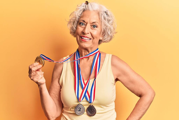 Starší šedovlasá žena s medailemi vypadá pozitivně a spokojeně a usmívá se s sebevědomým úsměvem vyceněným zuby  - Fotografie, Obrázek