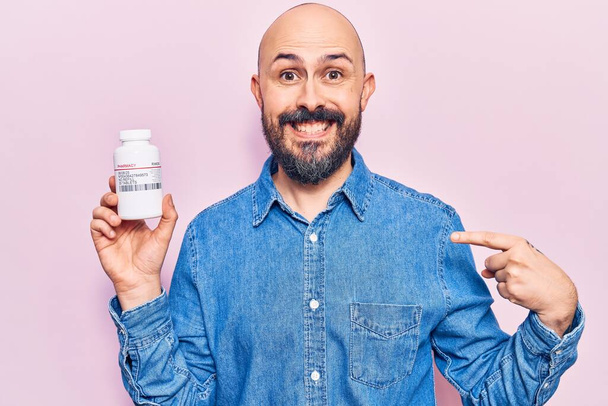 Jeune homme beau tenant des pilules pointant du doigt un sourire heureux et fier  - Photo, image
