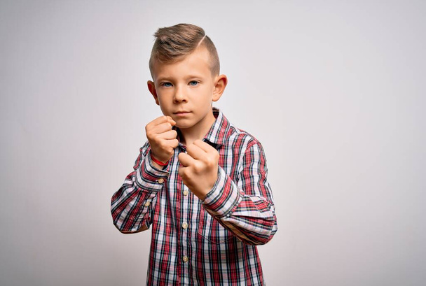 Молодий маленький кавказький хлопчик з блакитними очима в елегантній сорочці, що стоїть над ізольованим тлом Готовий боротися з жестом захисту кулака, злий і засмучений обличчям, боїться проблем
 - Фото, зображення