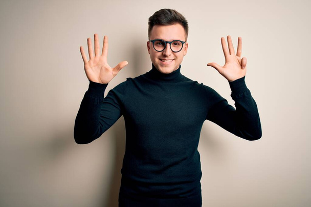 Young handsome caucasian man wearing glasses and casual sweater over isolated background showing and pointing up with fingers number nine while smiling confident and happy. - Foto, afbeelding
