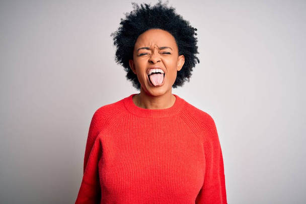 Young beautiful African American afro woman with curly hair wearing red casual sweater sticking tongue out happy with funny expression. Emotion concept. - Photo, Image