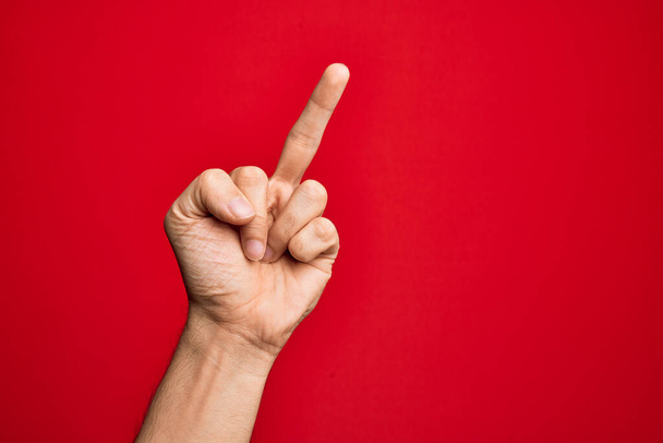 Mão de jovem caucasiano mostrando dedos sobre fundo vermelho isolado mostrando gesto provocante e rude fazendo foda você símbolo com o dedo médio
 - Foto, Imagem