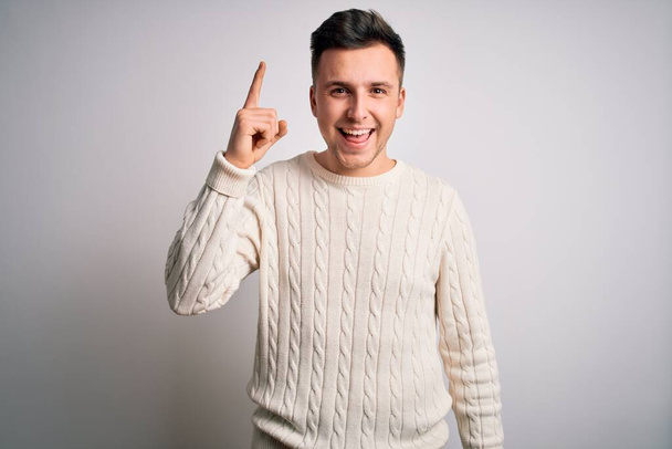 Young handsome caucasian man wearing casual winter sweater over white isolated background pointing finger up with successful idea. Exited and happy. Number one. - Photo, Image