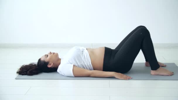 Health concept. Young pregnant woman does yoga exercise in the white room - Кадры, видео