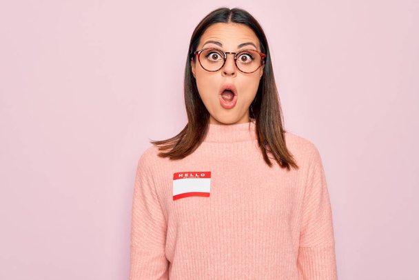 Young beautiful brunette woman wearing sticker with hello my name is message scared and amazed with open mouth for surprise, disbelief face - Photo, Image