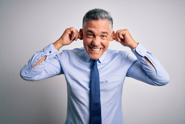 Homem de negócios bonito de cabelos grisalhos de meia idade vestindo camisa elegante e gravata Smiling puxando orelhas com os dedos, gesto engraçado. Problema de audição
 - Foto, Imagem