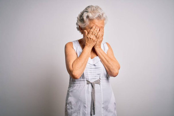Senior kaunis harmaa tukka nainen yllään rento kesämekko valkoisella taustalla surullinen ilme peittää kasvot kädet itkien. Masennuksen käsite. - Valokuva, kuva