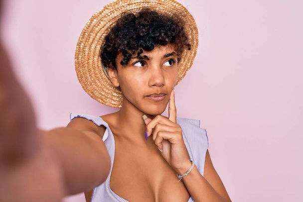 Güzel Afro-Amerikan turist kadın bikini giyiyor ve şapka takıyor. Kamera önünde selfie çekiyor. Ciddi bir yüz ifadesi var. - Fotoğraf, Görsel