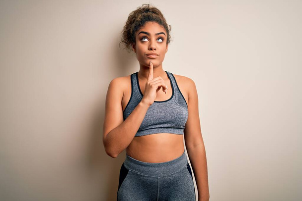 Young african american sportswoman doing sport wearing sportswear over white background Thinking concentrated about doubt with finger on chin and looking up wondering - Zdjęcie, obraz