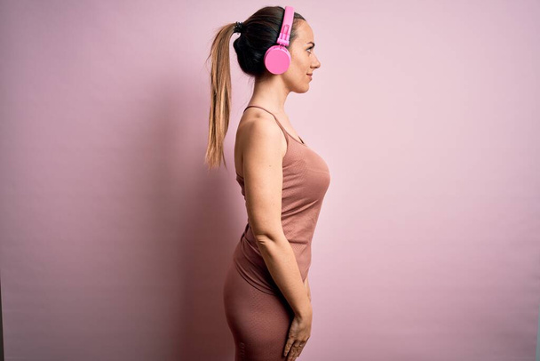Mujer joven fitness que usa ropa de entrenamiento deportivo que usa auriculares escuchando música mirando hacia un lado, pose de perfil relajado con cara natural con sonrisa confiada
. - Foto, Imagen