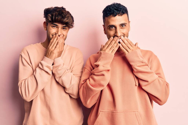 Young gay couple wearing casual clothes laughing and embarrassed giggle covering mouth with hands, gossip and scandal concept  - Fotografie, Obrázek