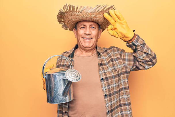 Senior man with grey hair wearing gardener hat holding watering can doing ok sign with fingers, smiling friendly gesturing excellent symbol  - 写真・画像