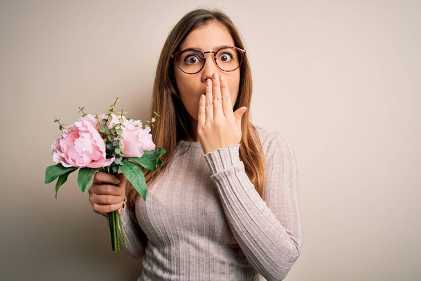 Young blonde woman holding beautiful romantic floral bouquet over isolated background cover mouth with hand shocked with shame for mistake, expression of fear, scared in silence, secret concept - Photo, Image