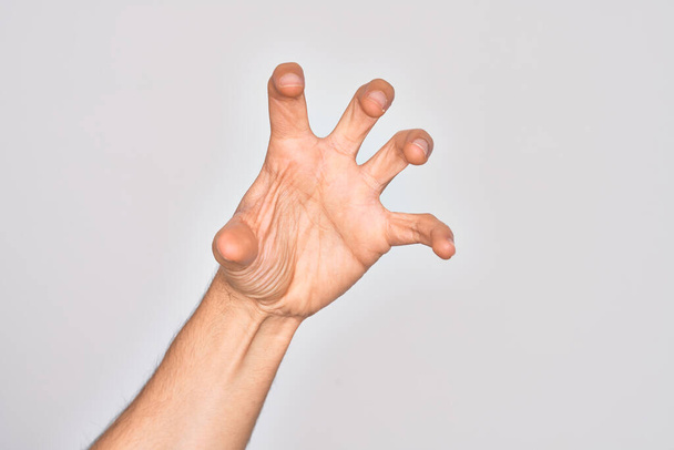 Hand of caucasian young man showing fingers over isolated white background grasping aggressive and scary with fingers, violence and frustration - Photo, Image